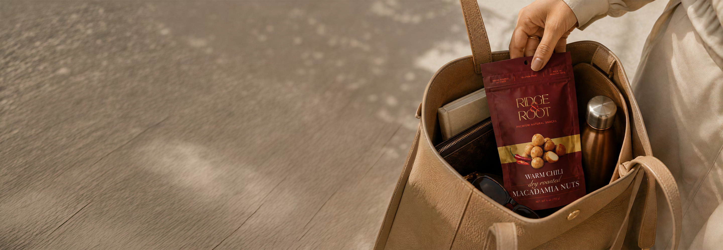 A hand placing a Warm Chili macadamia pouch into a tote bag