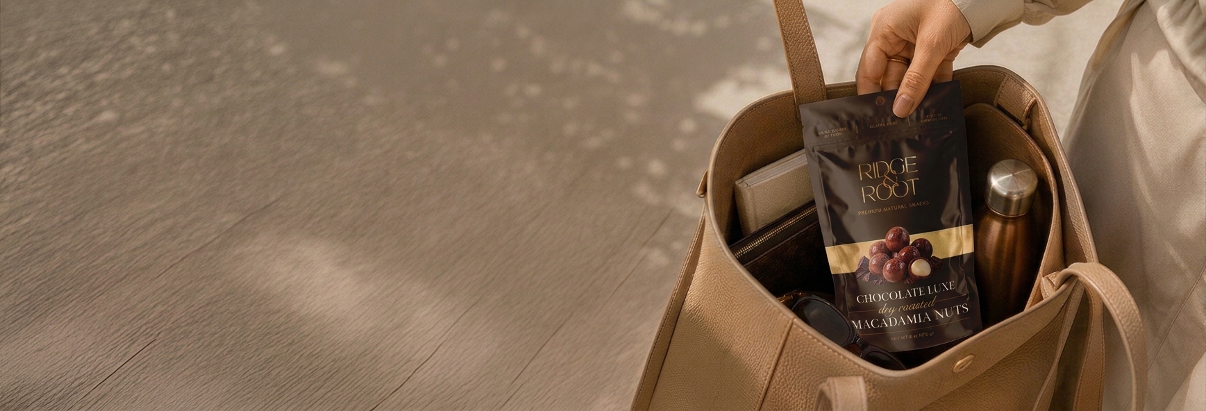 A hand holding a Chocolate Luxe Ridge & Root macadamia pouch over a canvas tote bag