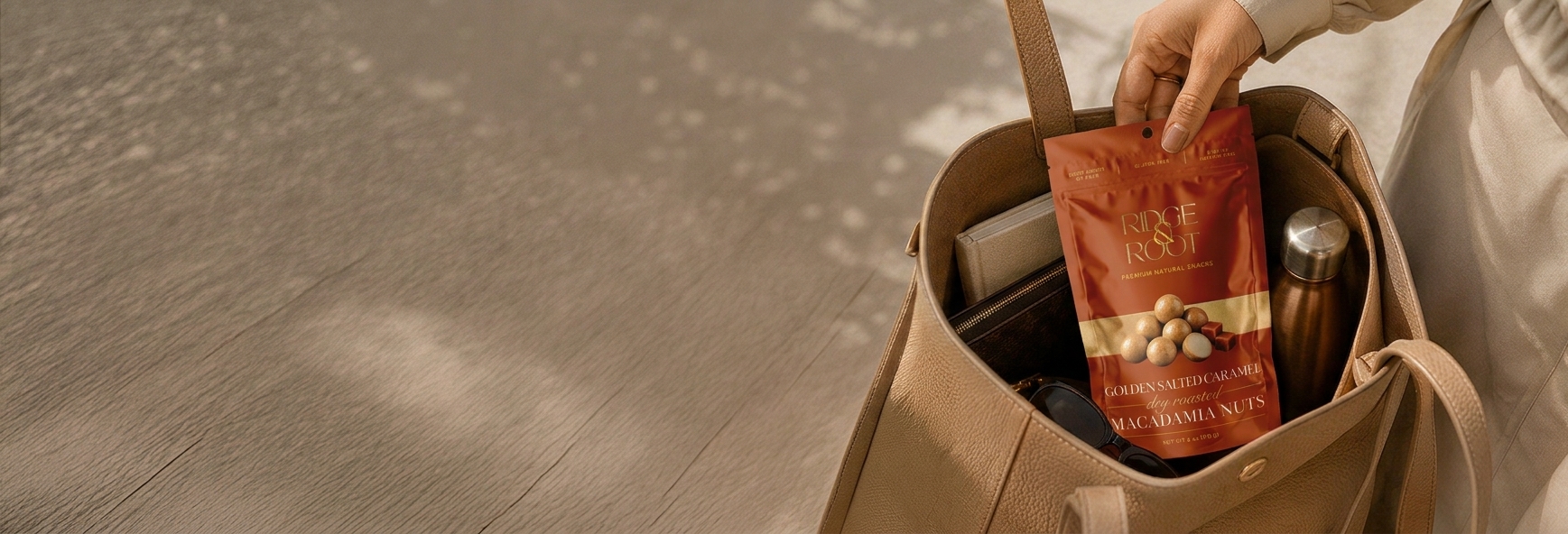 A hand holding a Golden Salted Caramel Ridge & Root macadamia pouch over a canvas tote bag